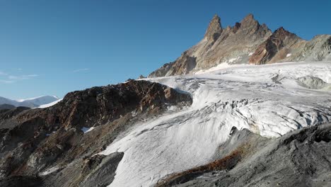 Luftaufnahme-Eines-Gletschers-In-Der-Nähe-Von-Arolla-Im-Wallis,-Schweiz-Mit-Den-Gipfeln-Der-Aiguilles-Rouges,-Die-Von-Der-Frühen-Morgensonne-Beleuchtet-Werden