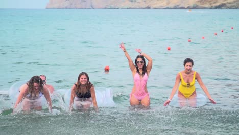 Group-of-Friends-Having-Fun-Splashing-Beach-Waters-with-Swim-Rings-in-the-Summer,-Slowmotion