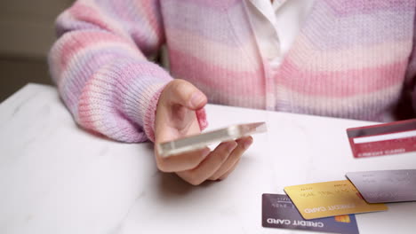 Close-up-woman's-hand-holds-a-smartphone-and-selects-a-mockup-Bank-credit-card-for-online-shopping-services-to-pay-money-with-cashless-technology