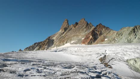 Luftüberflug-über-Einen-Gletscher-In-Der-Nähe-Von-Arolla-Im-Wallis,-Schweiz-Mit-Einem-Schwenk-Nach-Unten-Von-Den-Sonnenbeschienenen-Aiguilles-Rouges-Gipfeln-Bis-Zu-Den-Gletscherspalten-Im-Gletschereis