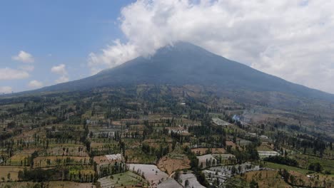 Tiny-agriculture-fields-and-massive-Mount-Sumbing-in-Indonesia,-aerial-view