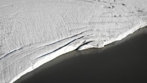 Aerial-flyover-alongside-the-ice-bordering-the-glacial-lake-of-the-Claridenfirn-glacier-in-Uri,-Swizerland-with-noticeable-crevasses-and-cracks-in-the-ice