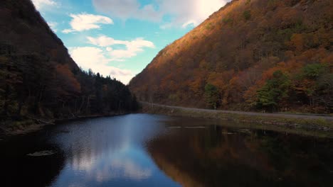 Stunning-low-drone-footage-over-a-small-pond-in-a-deep-autumnal,-colorful-mountain-valley