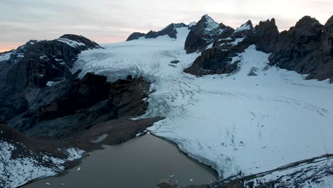 Vista-Aérea-Del-Lago-Glacial-Y-El-Hielo-Del-Glaciar-Claridenfirn-En-Uri,-Suiza-Al-Final-De-Un-Día-Con-Picos-Alpinos-Detrás-De-Una-Pared-De-Hielo-Y-Icebergs-Flotando-En-El-Agua