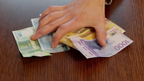 Person-pushes-Norwegian-banknotes-across-table-towards-camera,-slow-motion