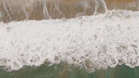 Aerial-Birds-Eye-View-Of-Foam-Ocean-Waves-Crashing-On-Beach