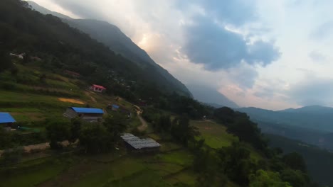 Aerial-FPV-drone-swoops-along-lush-cliff-in-Pokhara-Nepal-to-reveal-red-roof-school-buildings