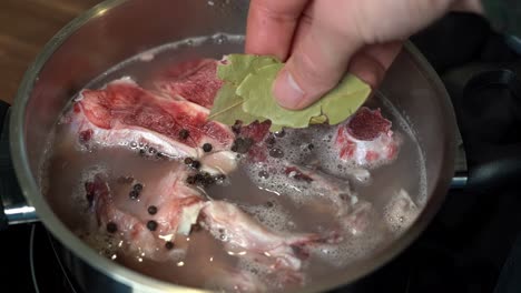 Dried-bay-leaf-added-to-pan-for-cooking-beef-bone-broth,-slow-motion