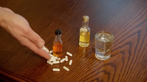 White-pills-falling-from-hand-to-wooden-table-with-alcohol,-slow-motion