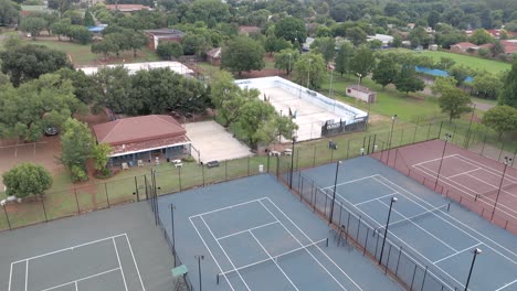 Langsame,-Nach-Rechts-Und-Nach-Oben-Geneigte-Luftaufnahme-Von-Den-Tennisplätzen-Eines-Alten-Tennisclubs,-Die-Den-Blick-Auf-Den-Rest-Der-Stadt-Freigibt