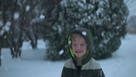 Young-happy,-smiling-boy-playing-in-the-snow-throwing-snowflakes-in-the-air-in-slow-motion