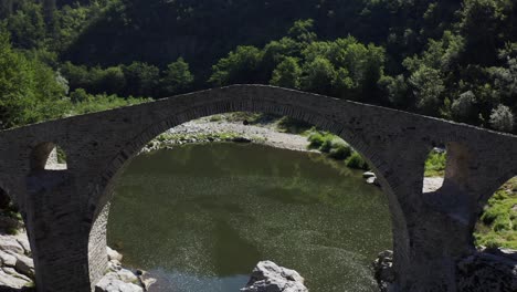Retreating-drone-shot-revealing-the-full-length-of-the-Devil's-Bridge-situated-in-Ardino-at-the-foot-of-Rhodope-Mountain-in-Bulgaria