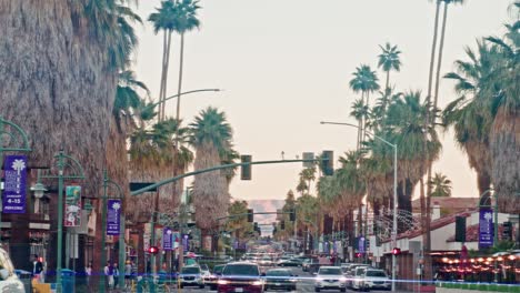 Tilt-down-from-palm-trees-to-cars-driving-in-downtown-Palm-Springs,-California-in-slow-motion-and-lens-flare-effect