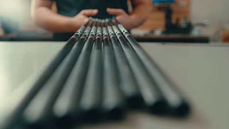 Male-hands-grab-set-of-golf-club-shafts-off-counter-top-in-workshop-in-slow-motion