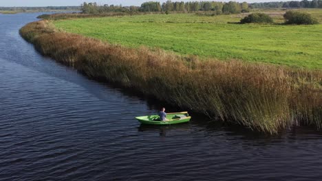 Circulating-drone-shot-with-man-on-fishing-boat-who-are-fishing-in-the-river-near-reeds