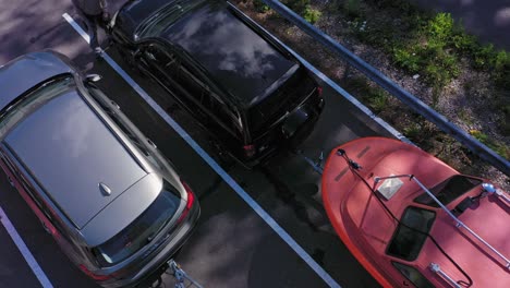 Aerial-view-away-from-a-parked-car-and-boat-trailer,-on-a-parking-lot,-in-Scandinavia---tilt-up,-drone-shot