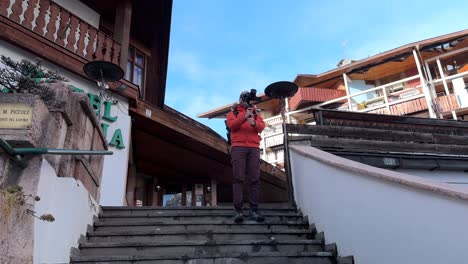 Travel-Photographer-With-Camera-On-Gimbal-Stabilizer-Standing-On-Stairs,-Taking-Photos-In-Cortina-d'Ampezzo,-Italy