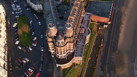 Aerial-top-shot-of-The-Grand-Hotel-with-some-vehicles-parked-on-road-beside-it-during-sunny-day-in-Scarborough-North-Yorkshire,-England
