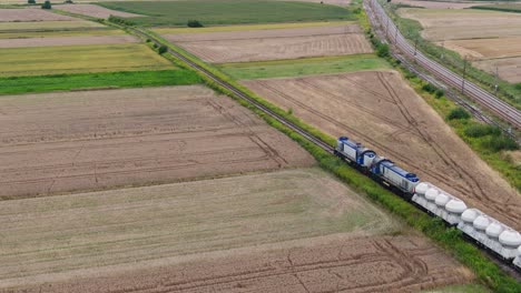 Locomotives-with-freight-wagons-move-through-wheat-fields,-transport-train-aerial-view