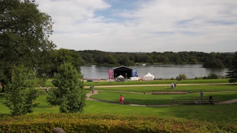 Families-And-Kids-In-Trentham-Gardens,-Stage-By-The-Lake-Set-Up-For-Concerts