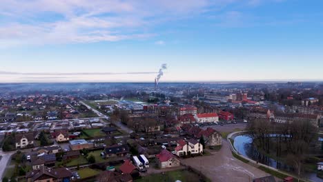 Aerial-panoramic-establish-of-small-european-town-with-large-smokestack-in-distance-under-blue-sky