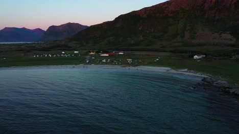 Aerial-view-of-the-Hovsvika-beach,-the-Hov-horse-farm-and-camping,-during-dusk-in-Gimsoya,-Norway---rising,-drone-shot