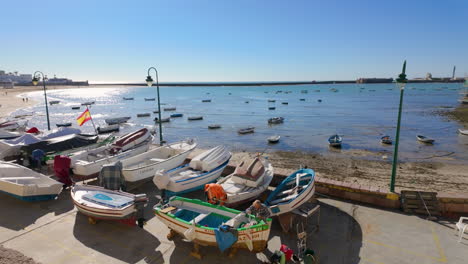 Pequeños-Barcos-Amarrados-En-La-Orilla-Con-El-Océano-Al-Fondo-En-Cádiz,-España.