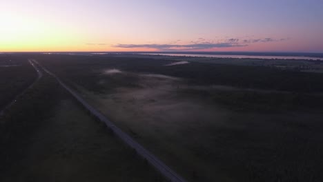 Am-Späten-Abend-Schoss-Eine-Drohne-Bei-Sonnenuntergang-über-Die-Autobahn,-Wobei-Tief-Liegender-Nebel-Die-Bäume-Bedeckte