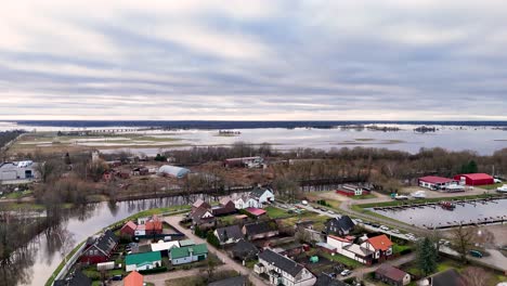 Aftermath-of-winter-flooding-in-town-outskirts-of-Silute-Lithuania,-calm-water-reflects-sky-and-leafless-trees