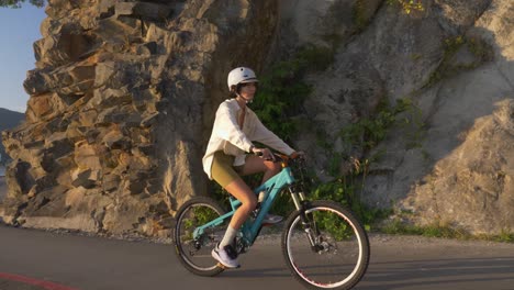 Sportliches-Mädchen-Mit-Helm-Beim-Fahrradfahren-über-Die-Straße-Durch-Felsklippen