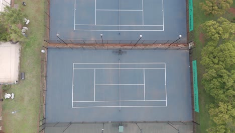 Drohnenaufnahme-Aus-Der-Vogelperspektive-Von-Oben-Auf-Alte-Tennisplätze-Mit-Verschiedenen-Farben-In-Einem-Wohn-Tennisclub