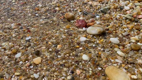 Waves-hitting-beautiful-colourful-natural-stones-rocks-sand-in-sea-water-at-the-beach-in-Cavalière-Lavandou-South-of-France,-nature-holiday-vacation,-4K-static-shot