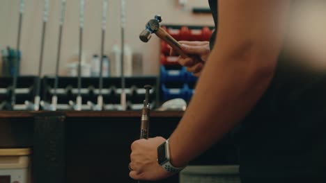 Male-hands-hammer-nail-into-golf-club-shaft-for-custom-fitting-in-workshop-in-slow-motion