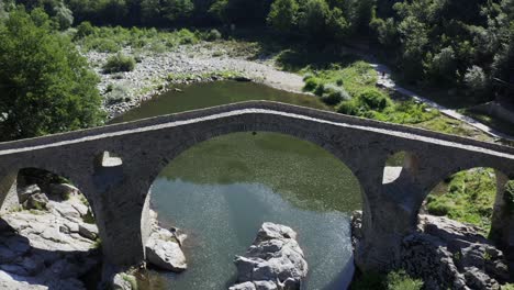 Tilting-drone-shot-revealing-the-front-view-of-the-Devil's-Bridge-located-in-Ardino-at-the-foot-of-Rhodope-Mountain-in-Bulgaria