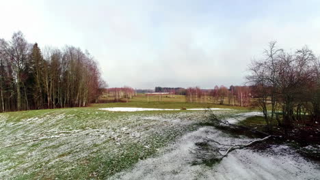 Early-winter-snow-over-a-countryside-field-of-grass-and-trees---aerial-flyover