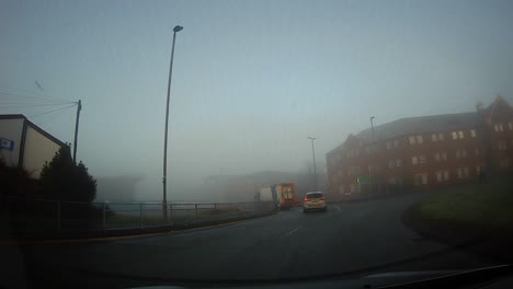 Foggy-POV-windshield-view-driving-misty-in-morning-town-traffic-roundabout-during-sunrise