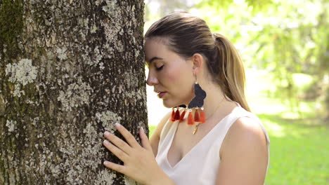 Close-up-of-girl-hugs-and-touches-a-tree-while-meditates-and-pray-in-the-forest