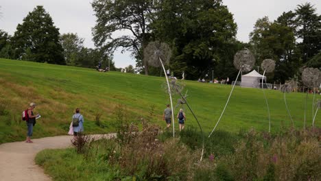 Wire-Fairy-And-Dandelion-Sculptures-In-The-Trentham-Gardens,-People-Walking-And-Relaxing