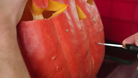 Knife-carving-a-creepy-smile-on-big-pumpking-for-Halloween-decoration,-spooky-Jack-o-lantern-decor-close-up