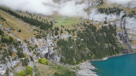 Drone-shots-of-Öschinensee-near-Kandersteg-in-Switzerland-with-turquoise-water-in-direction-of-the-massive-mountain-wall