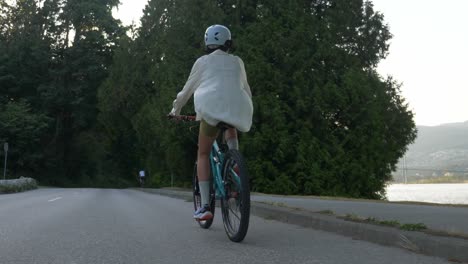 Siguiendo-A-Una-Mujer-En-Bicicleta-Por-La-Carretera-A-Lo-Largo-De-Burrard-Inlet-En-Vancouver,-Canadá