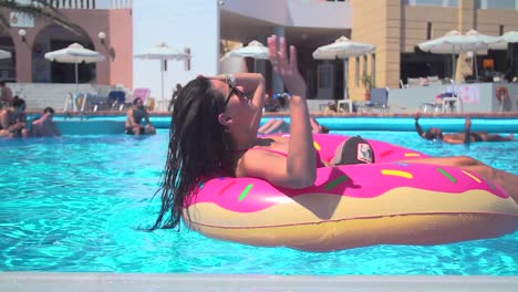Mädchen-Sonnt-Sich-Mit-Sonnenbrille-Und-Schwimmt-Mit-Einem-Donut-Format-In-Einem-Pool,-Zeitlupe