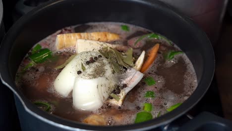 Beef-bone-broth-pan-with-herbs-and-vegetables-slowly-starts-simmering,-slow-motion