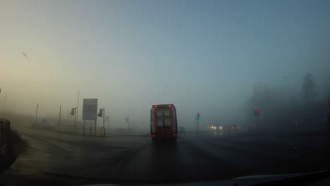 POV-Foggy-windshield-view-driving-through-misty-morning-town-traffic-roundabout-during-sunrise