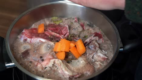 Fresh-orange-carrots-added-to-bone-broth-pan,-in-close-up-slow-motion