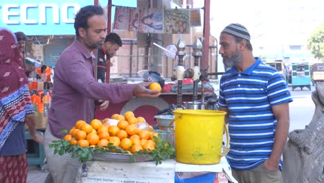 Closeup-shot-of-a-shopkeeper-selling-oranges-to-customers-during-daytime-beside-busy-Saddar-Bazar-Street-of-Karachi,-Pakistan