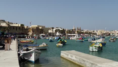 Schwimmende-Boote-In-Der-Nähe-Der-Strandpromenade-Im-Hafen-Von-Marsaxlokk