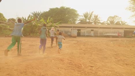 Glückliche-Afrikanische-Schwarze-Kinder,-Die-Zusammen-Spielen-Und-Bei-Sonnenuntergang-Auf-Der-Staubigen-Straße-Eines-Abgelegenen-Ländlichen-Dorfes-Laufen