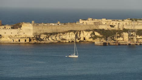 Small-Boat-Sailing-In-The-Grand-Harbour-With-Fort-Ricasoli-In-The-Background