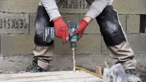 Construction-worker-using-power-drill-to-make-big-hole-into-wood-plank-corner-wearing-gloves,-Medium-shot
